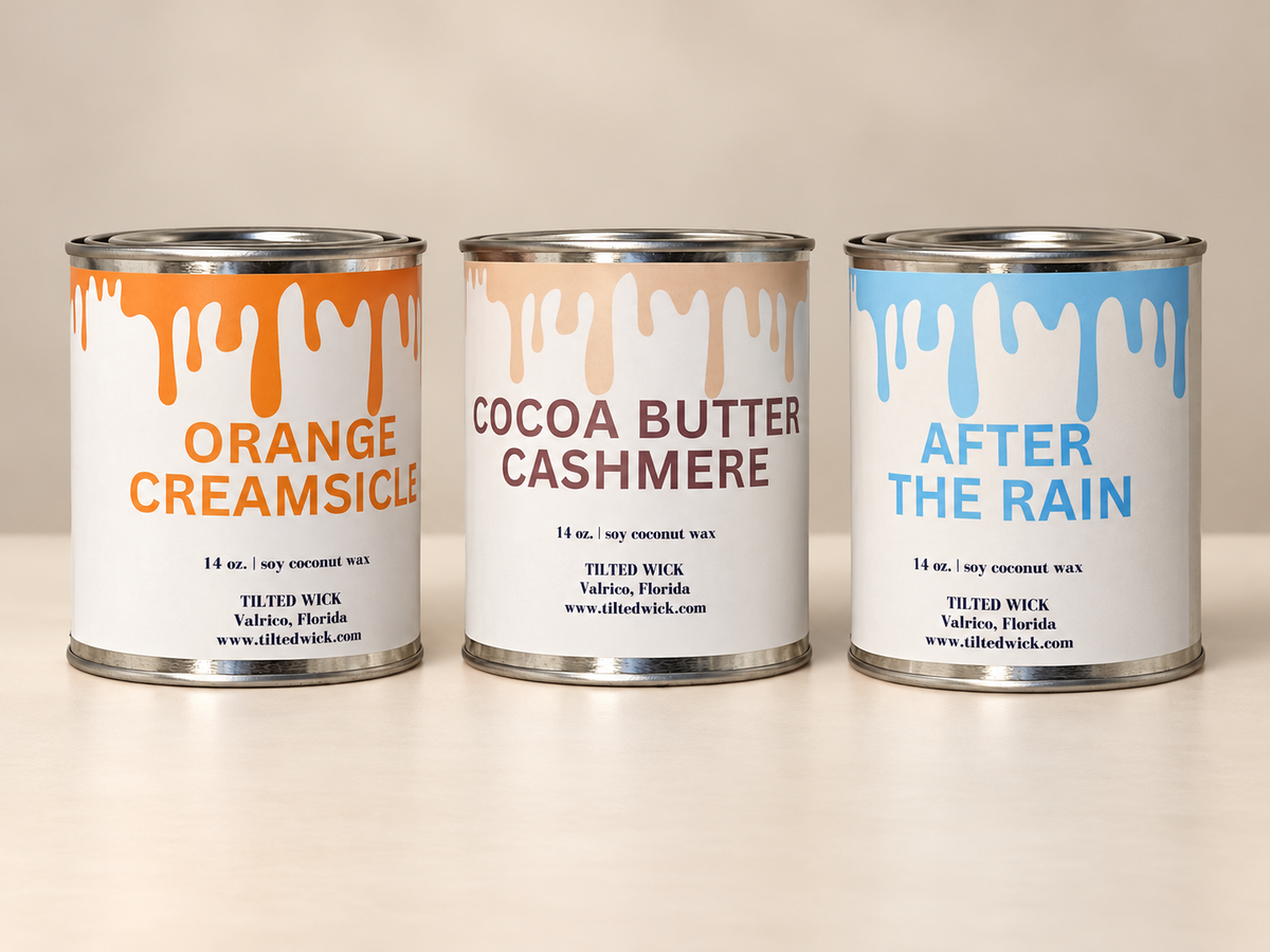 Three 14-ounce paint tin candles in Orange Creamsicle, Cocoa Butter Cashmere, and After the Rain on a neutral studio backdrop